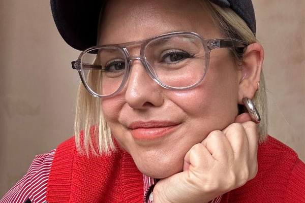 Lady wears glasses and a black hat, with a striped red shirt and a red tank top, along with some silver hoop earrings.