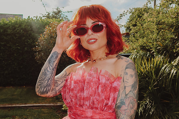 Women with red hair in a pink dress wearing red framed sunglasses
